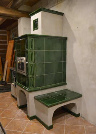 Kachlový sporák s prosklenými dvířky a topeništěm UMWELT PLUS. Sporák také temperuje koupelnu umístěnou za  zády sporáku.